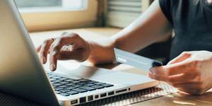 close up of a laptop and desk with a persons hands typing in a credit card number