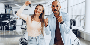 an excited couple smiling at the dealership and showing the keys to their new car